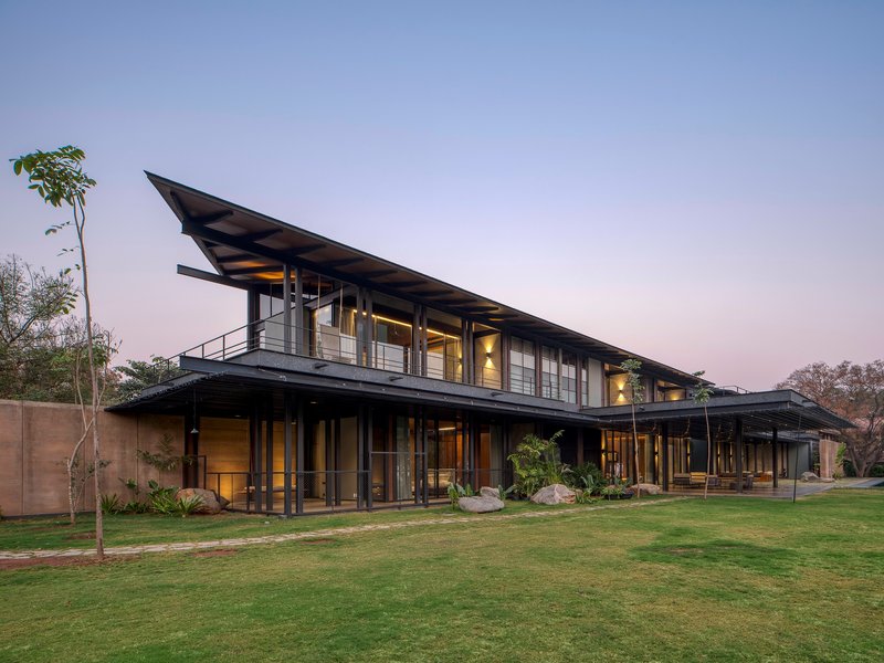 Two-story residence with extended metal roof planes and glazed facades overlooking a manicured lawn at dusk