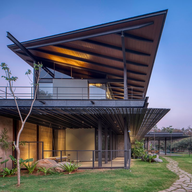 Corner view showing the cantilevered upper balcony with steel columns and horizontal sun louvers below at twilight