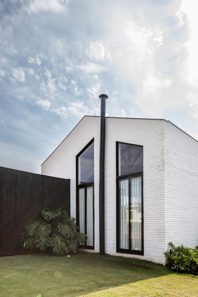 White-painted brick volume with tall black-framed windows and a dark metal flue pipe under cloudy skies