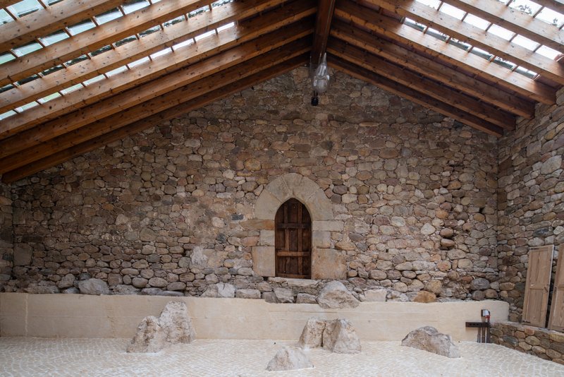 Stone gable end wall with arched timber door and exposed roof rafters above excavated floor level