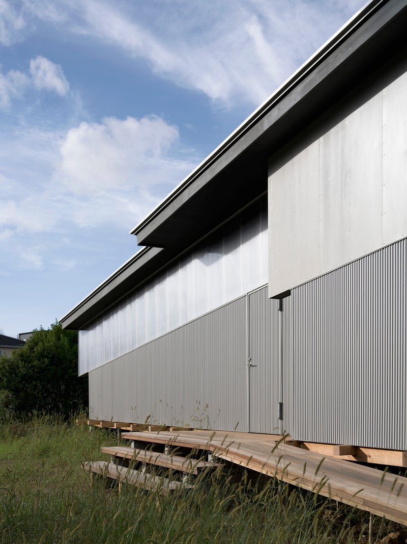 Corrugated metal facade with timber deck elevated on concrete blocks beneath a blue sky