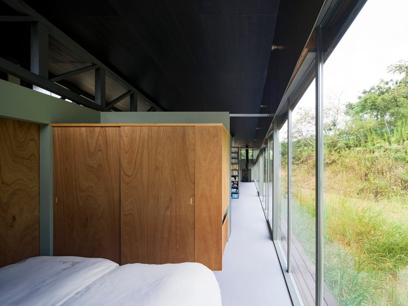Bedroom with timber wardrobe and full-height glazing overlooking meadow grasses in afternoon light