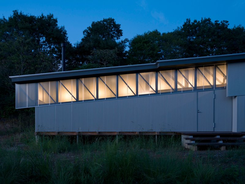 Illuminated facade with exposed diagonal timber framing and corrugated metal cladding at dusk