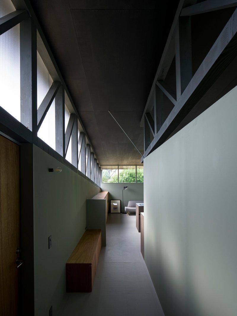Corridor with exposed diagonal timber bracing overhead and pale green walls leading to seating area
