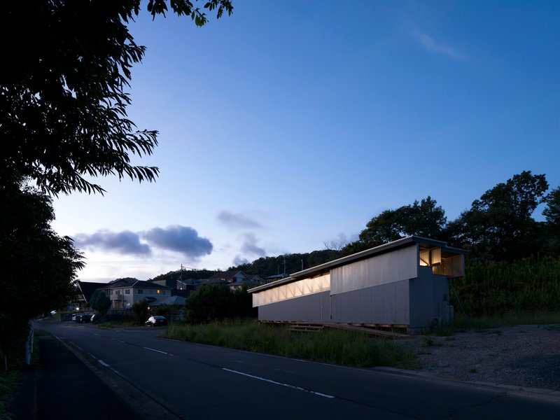 Street view of the residence with illuminated clerestory windows at dusk beneath wooded hillside
