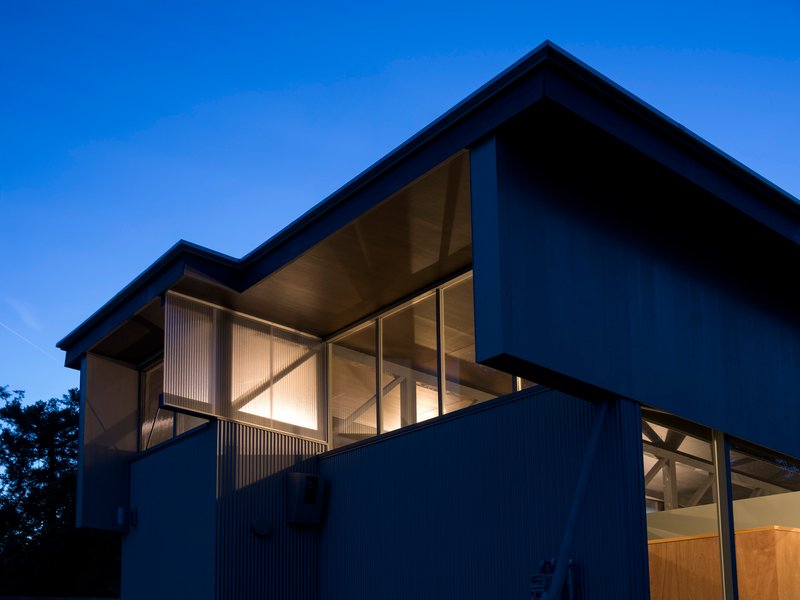 Corner view of the cantilevered upper volume with diagonal braced glazing at twilight