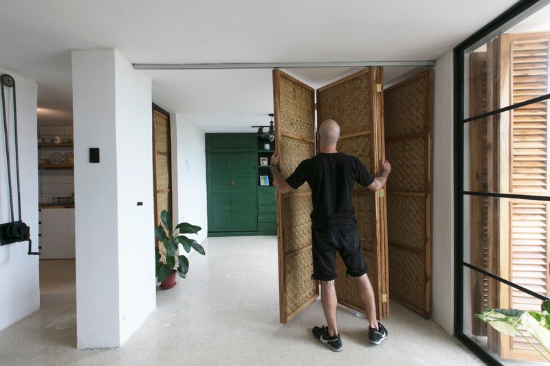 Person adjusting folding woven screen panels in a white-walled interior with polished concrete floor