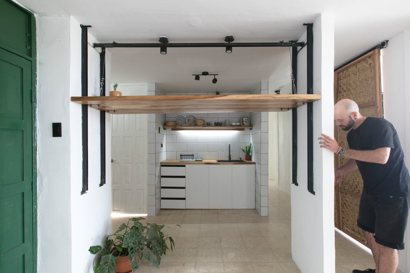 Kitchen alcove with white tile backsplash framed by black steel columns and a timber shelf overhead