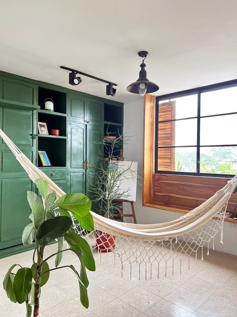 Interior room with green built-in shelving, hammock and large black-framed window overlooking greenery