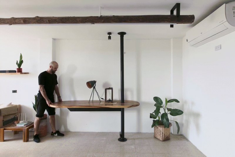 Living room with a fold-down timber table suspended from a black vertical pipe column