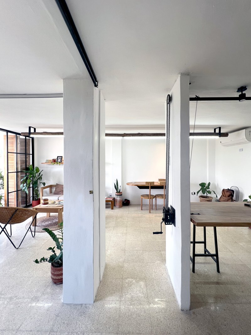 Open loft space with white columns, exposed black beams, steel-framed glazing, and terrazzo flooring