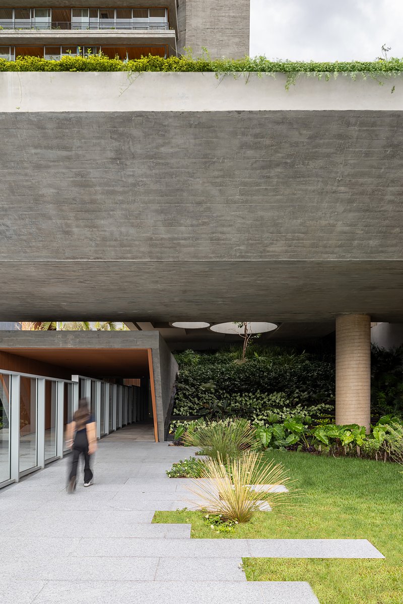 Board-formed concrete soffit above entry with figure walking past planted courtyard and timber screens