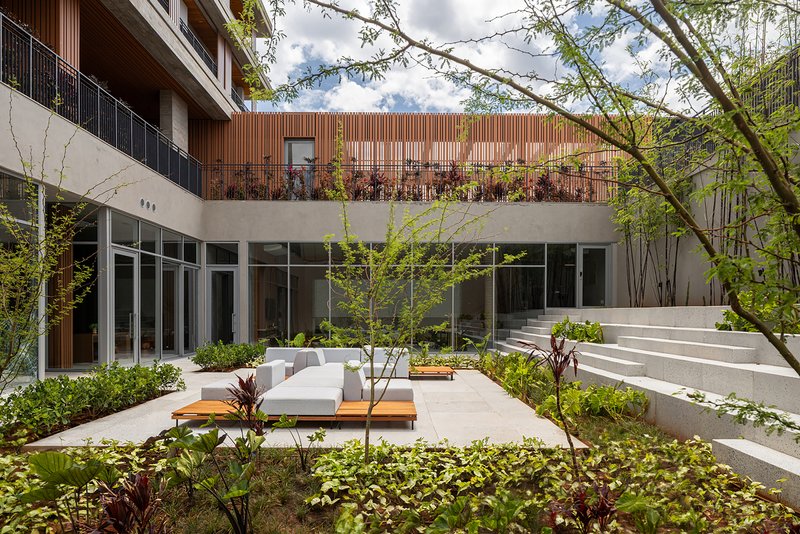 Interior courtyard with planted beds, white benches and stepped seating beneath vertical timber-clad volume