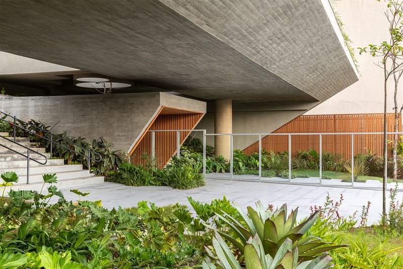 Textured board-formed concrete ceiling cantilever over entry plaza with tropical plantings in foreground