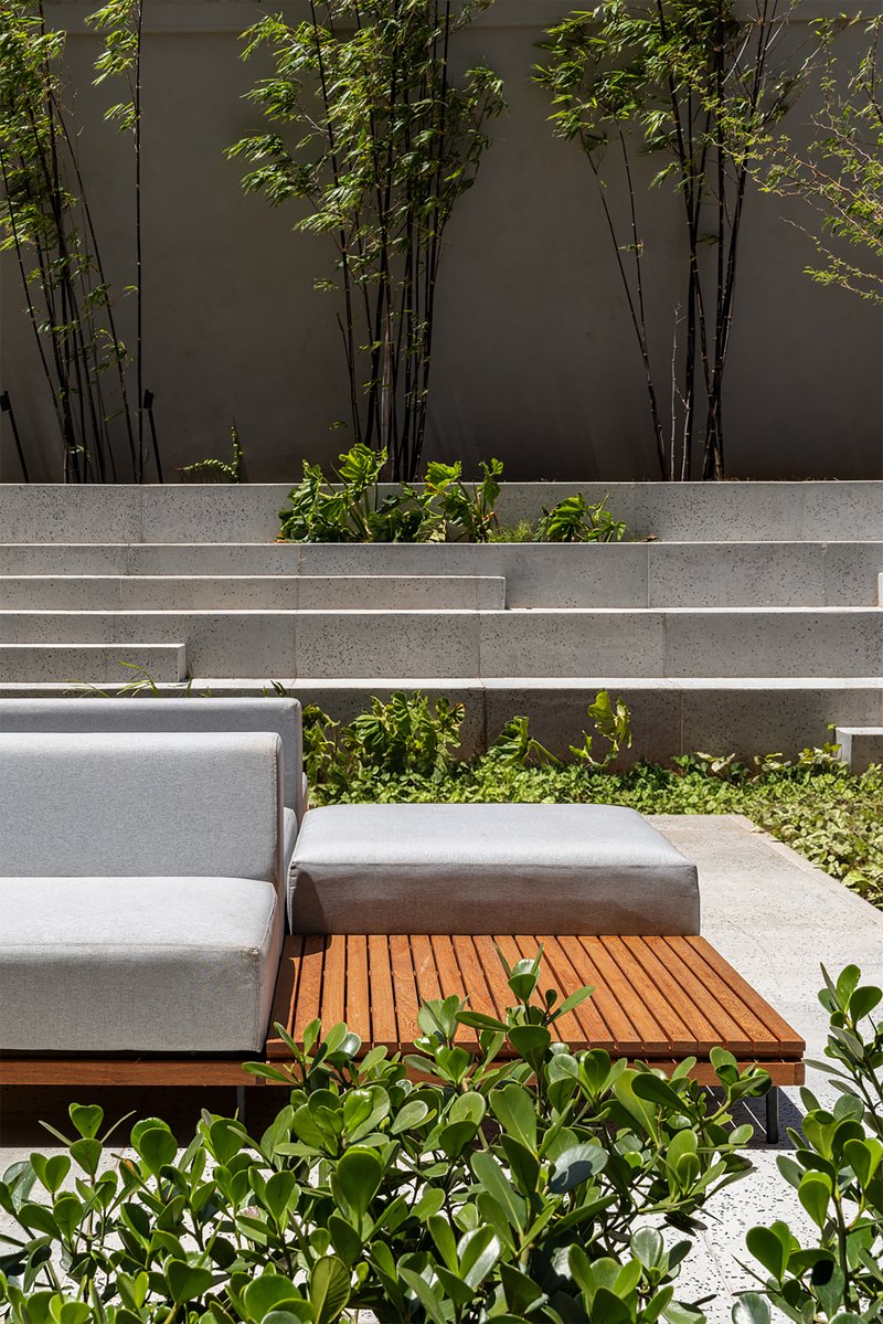 Close-up of timber-deck seating module with cushions beside concrete steps and bamboo planting