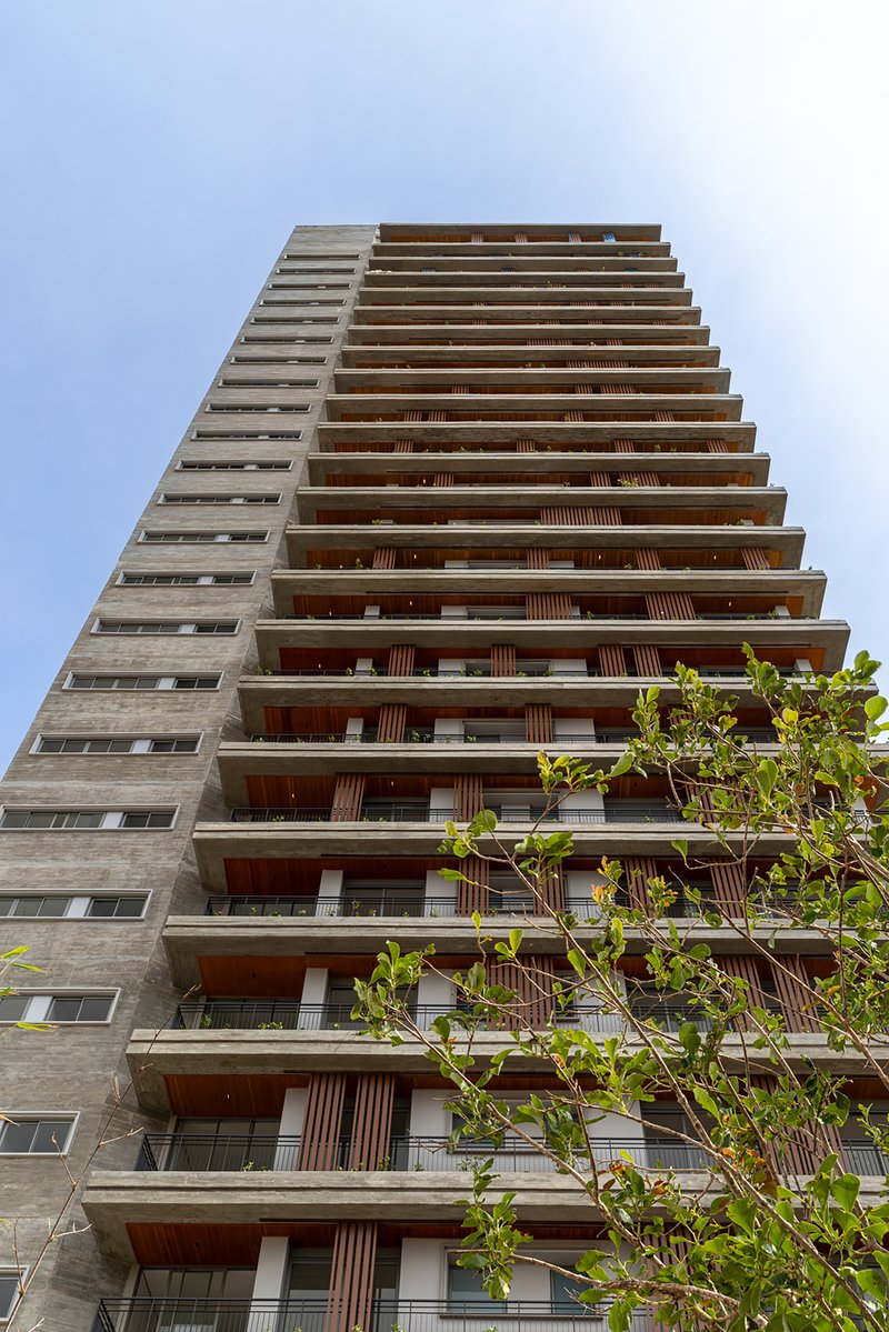 Upward view of residential tower facade with alternating concrete fins and timber-screened balconies against pale sky