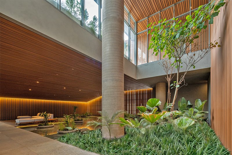 Double-height atrium with circular concrete column, planted beds, and clerestory glazing admitting daylight