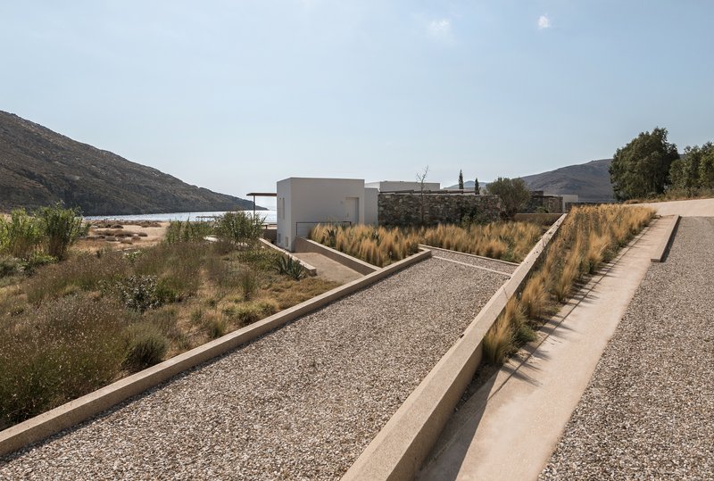 Stepped concrete pathway with gravel fill and ornamental grasses leading toward white volumes and distant hills