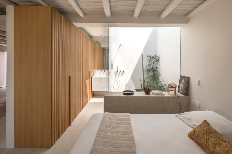 Bedroom interior with vertical timber slat partition and open courtyard bathroom beyond exposed beam ceiling