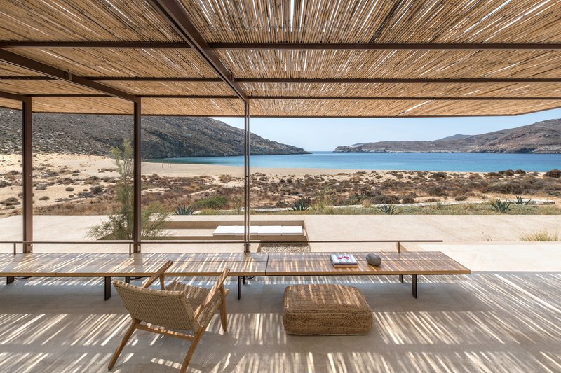 Long dining table under woven reed ceiling with view across coastal terrain to bay