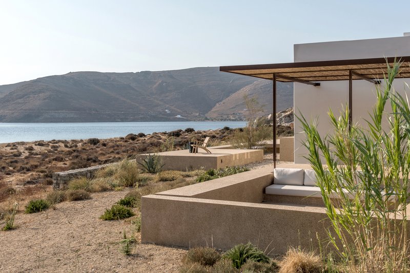 Terraced concrete seating platforms with canopy shelter framing coastal scrubland and calm bay