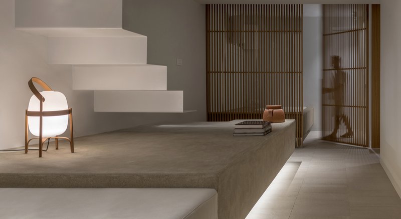 Cantilevered white plaster stairs with curved timber chair beneath and slatted wooden screens behind raised platform