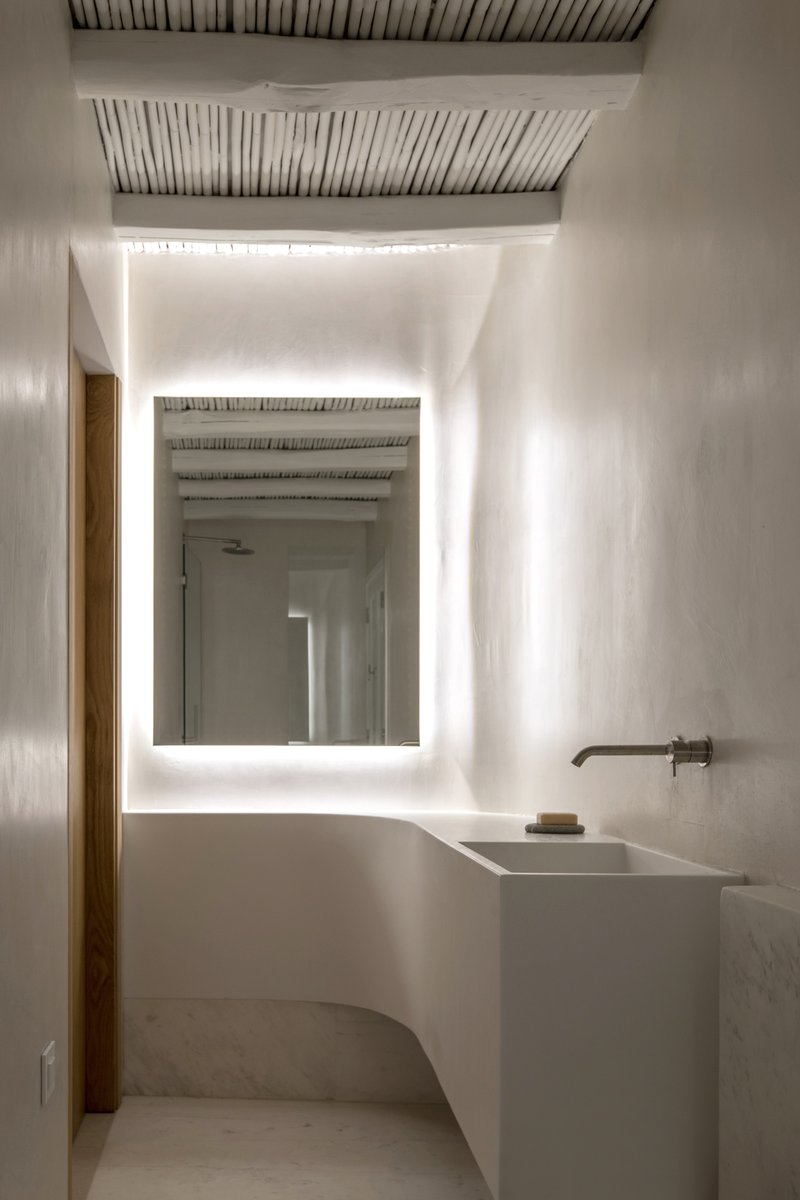 Bathroom with backlit mirror and white plaster vanity under exposed timber slat ceiling and indirect cove lighting