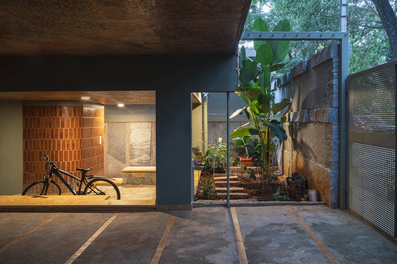 Ground-level courtyard with bicycle storage niche, perforated metal gate and banana plants at dusk