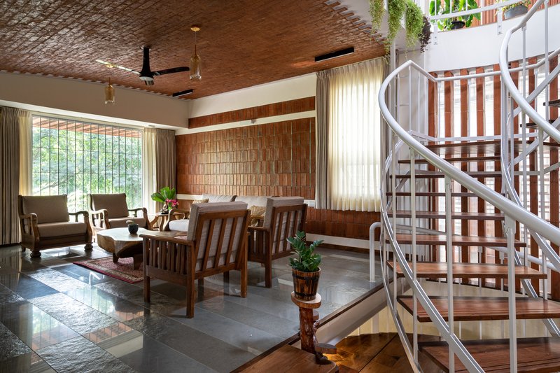 Living area with spiral metal staircase, brick ceiling, and upholstered chairs near a garden window