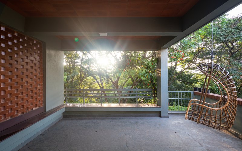 Open terrace with chequered brick screen wall, concrete soffit and wicker chair facing treetops