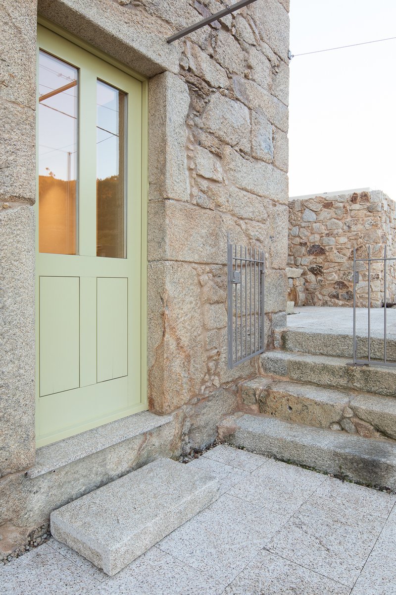 Pale green timber door set into granite wall beside granite steps and metal railing