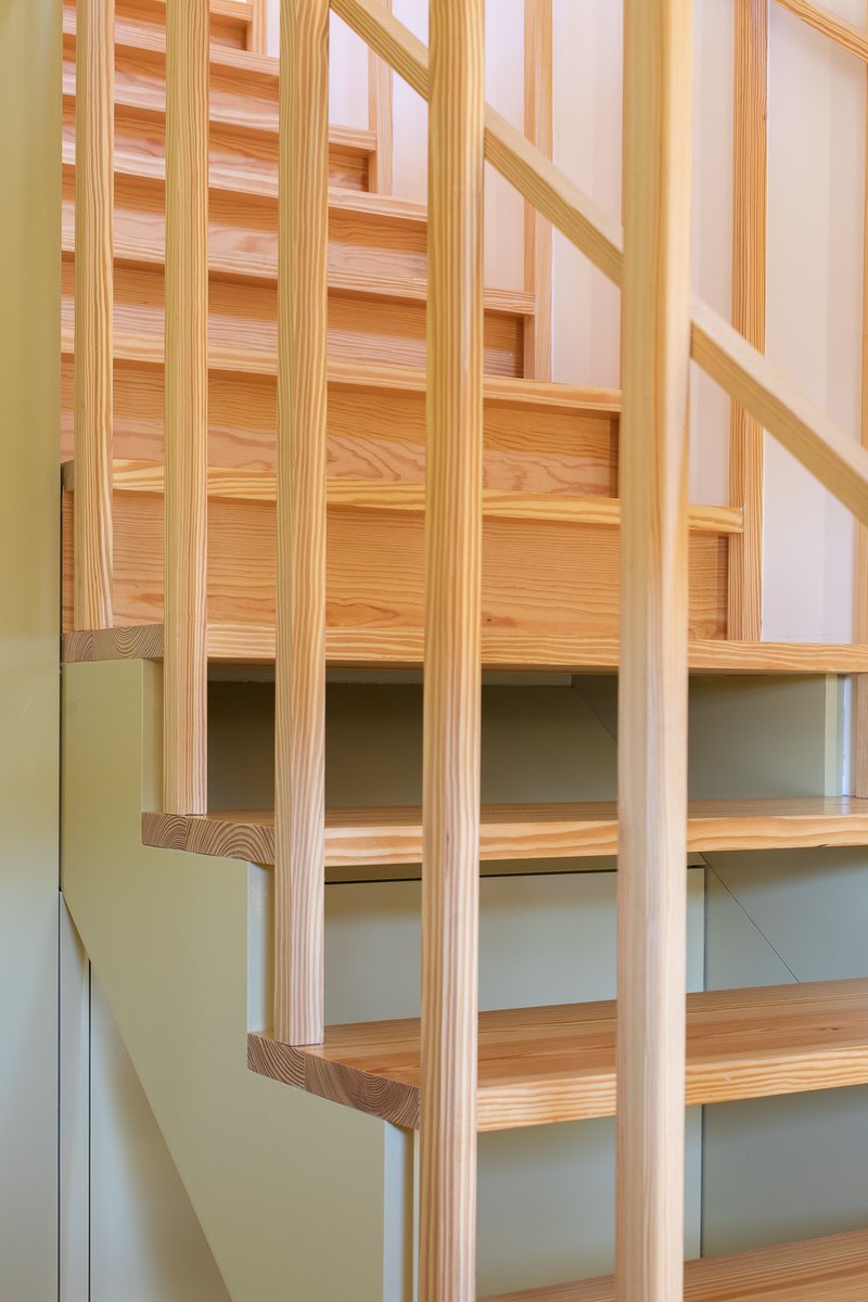 Timber staircase with vertical balustrade slats and open treads against a pale green wall