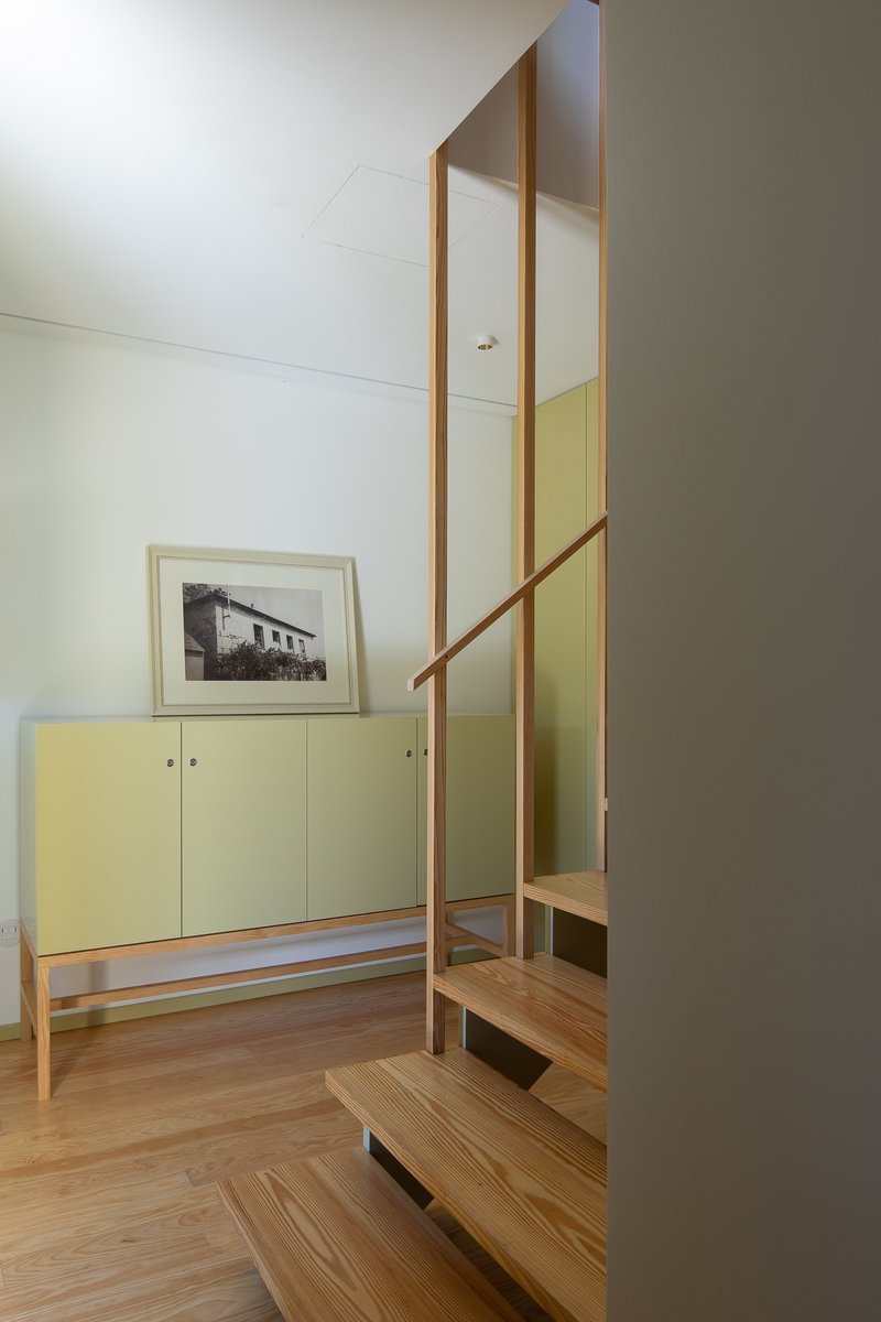 Open timber staircase ascending beside pale green built-in cabinetry and a framed photograph
