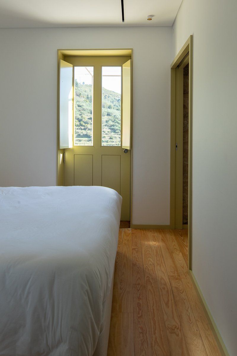 Bedroom with pale green window frame overlooking hillside vegetation in daylight