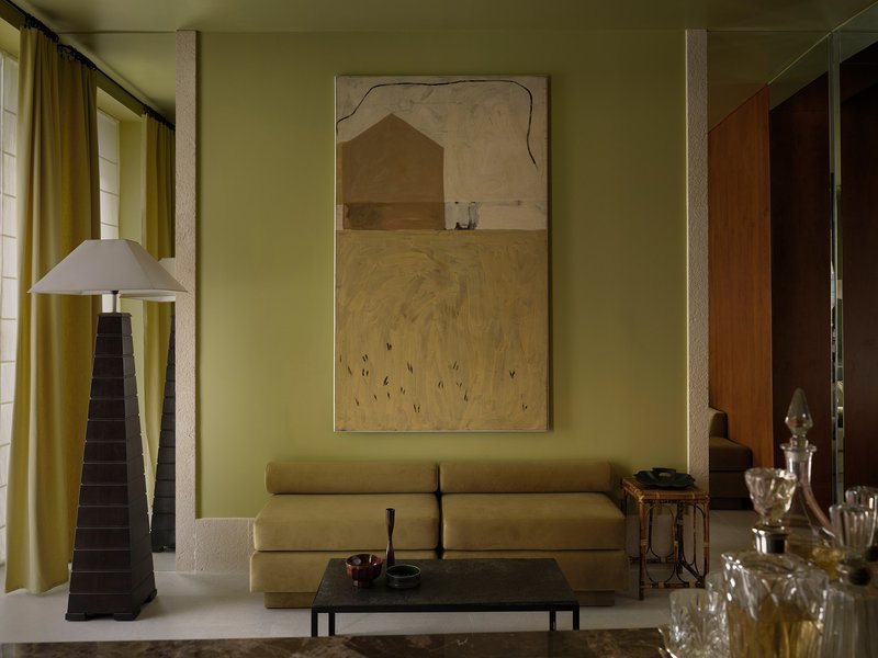 Living room with olive green walls, textured columns, and a pyramidal floor lamp beside yellow curtains