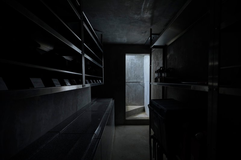 Dark interior corridor with steel shelving along walls and doorway backlit by diffused light