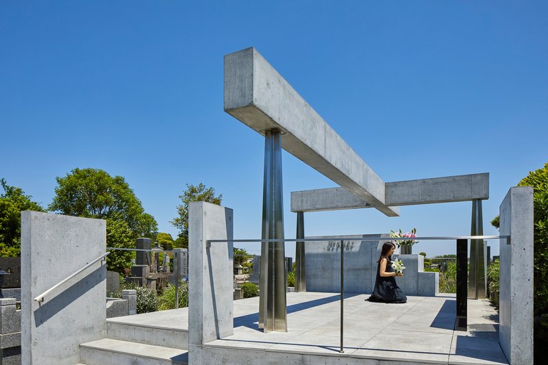 Person kneeling on concrete platform beneath intersecting beams and steel columns with glass balustrade