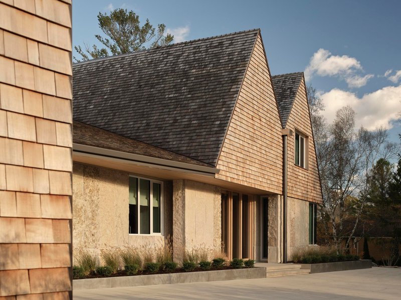 Side elevation showing the layered gable roofs with cedar shingles above textured rammed earth walls