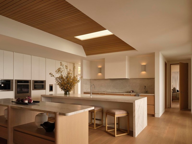 Kitchen with timber ceiling panels, central island, and integrated dining table under skylight
