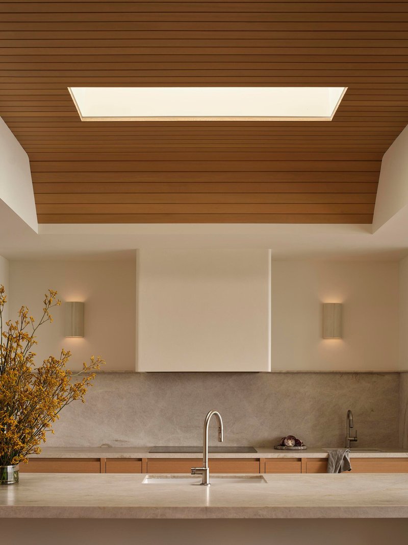 Kitchen island with stone countertop under a timber ceiling panel with integrated skylight