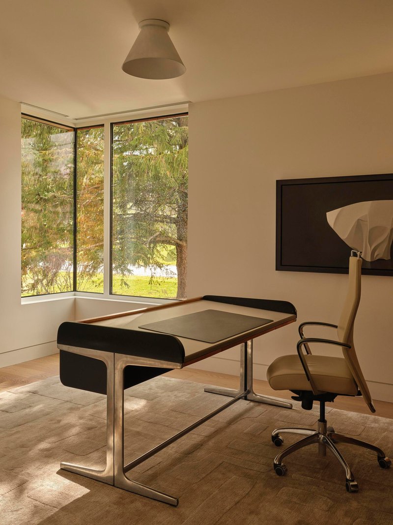 Corner study with black-framed desk and tall window overlooking trees in afternoon light
