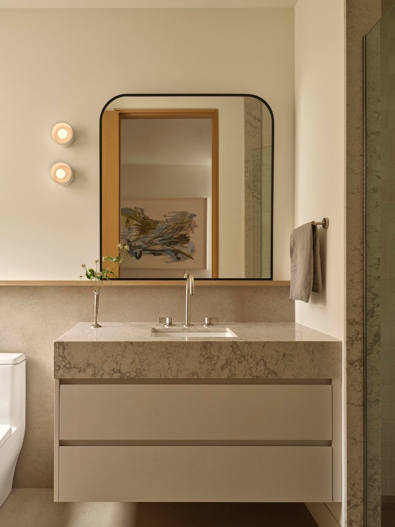 Floating vanity with thick stone countertop beneath a rounded-corner mirror and two circular wall sconces