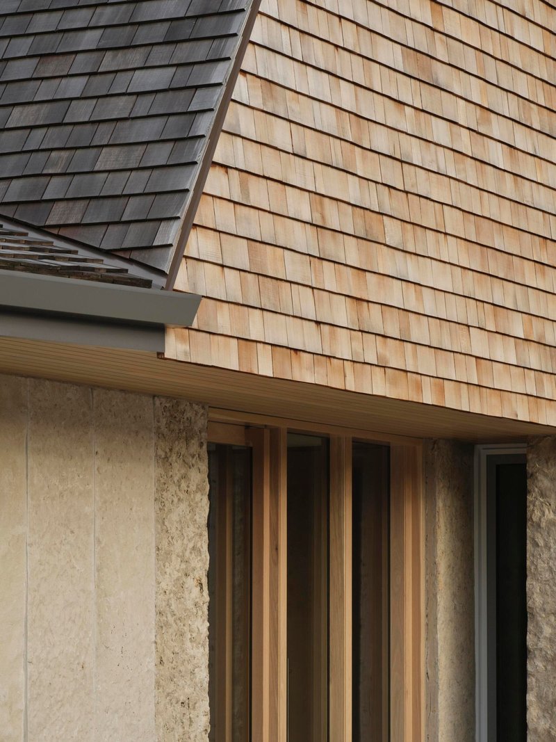 Detail of wood shingle cladding meeting a stone base below a timber-framed window