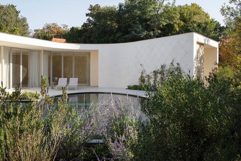 Exterior terrace with dark pool and lavender plantings below the glass-walled pavilion and curved white wall