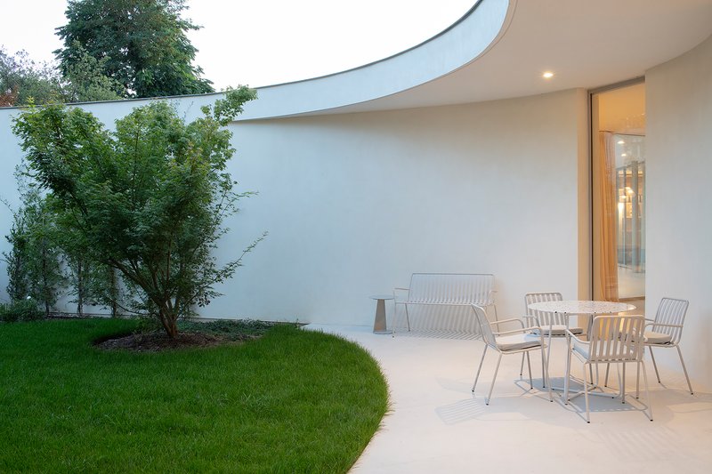 Curved courtyard wall with terrace seating and lawn under dusk lighting