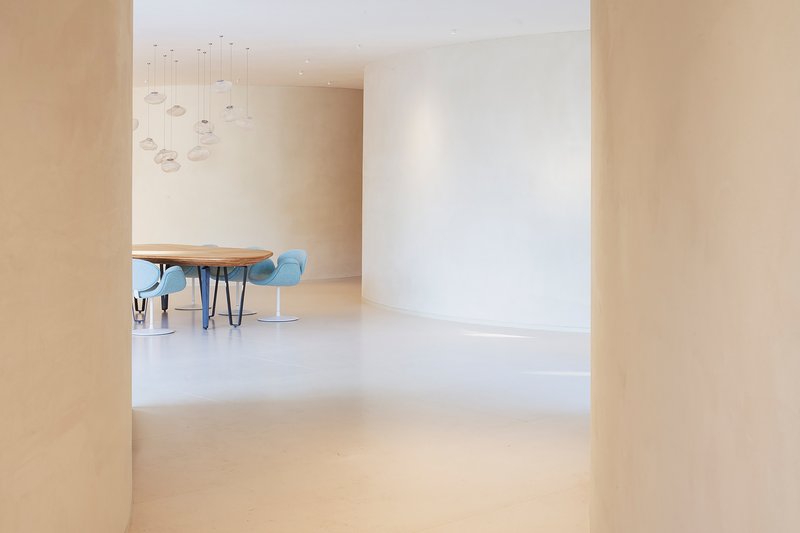 View through curved opening to dining area with pale plaster walls and polished floor