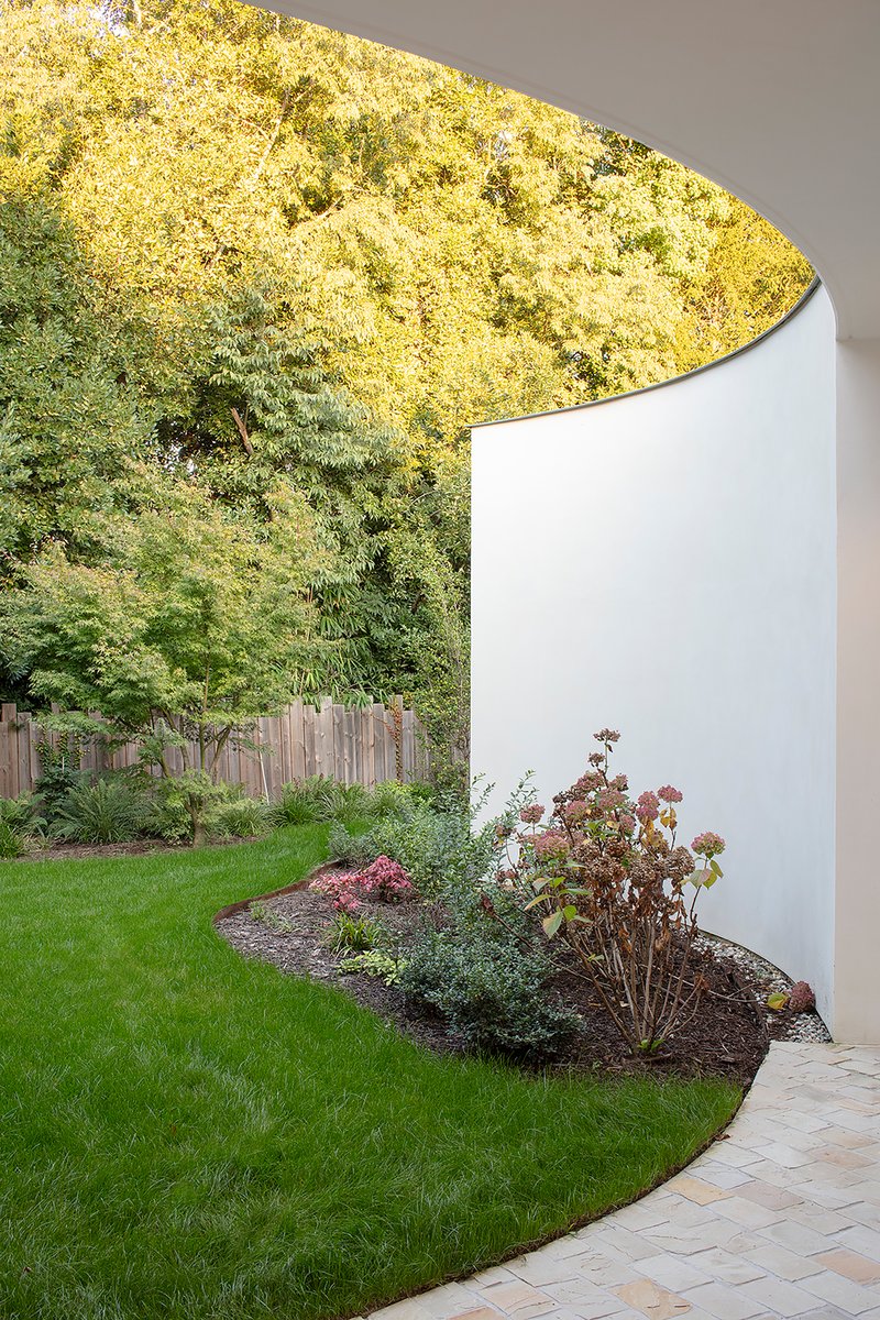 Curved white wall meeting a planted bed and lawn beneath autumn trees