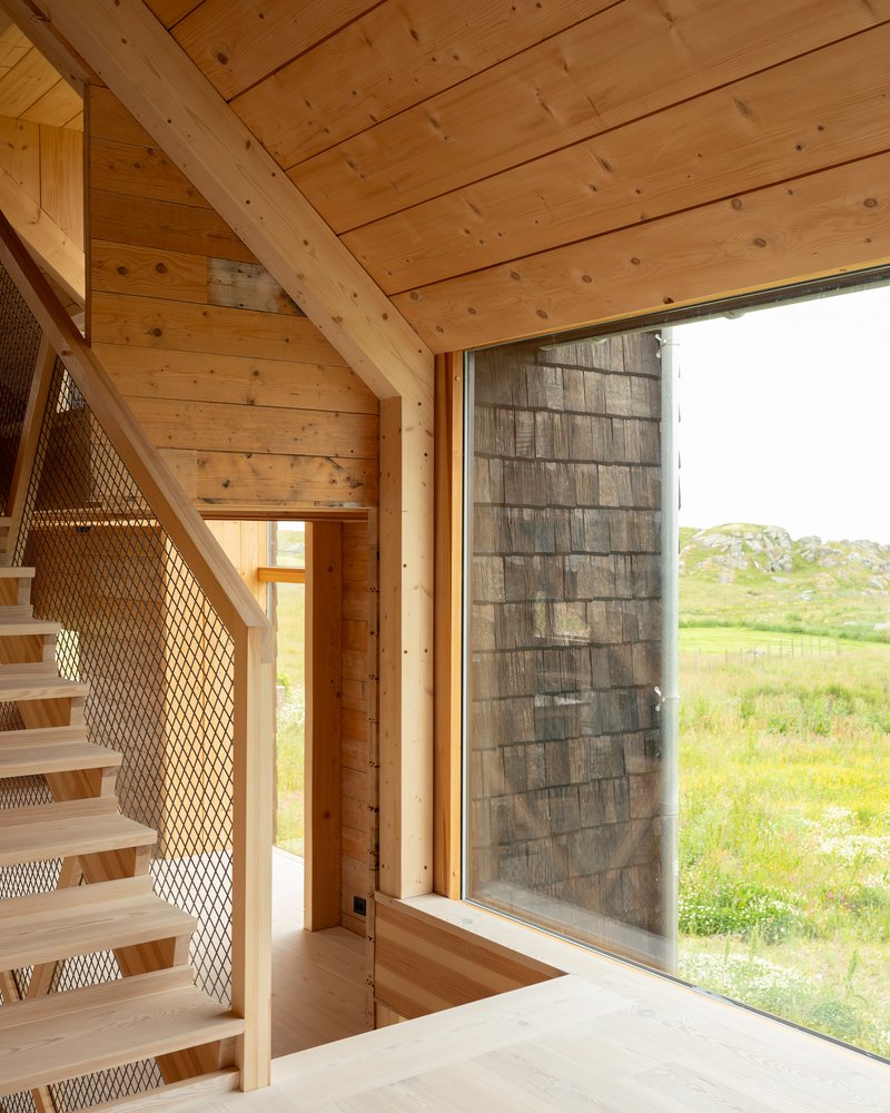 Open stair with mesh guardrail next to full-height glazing overlooking green meadow under overcast sky