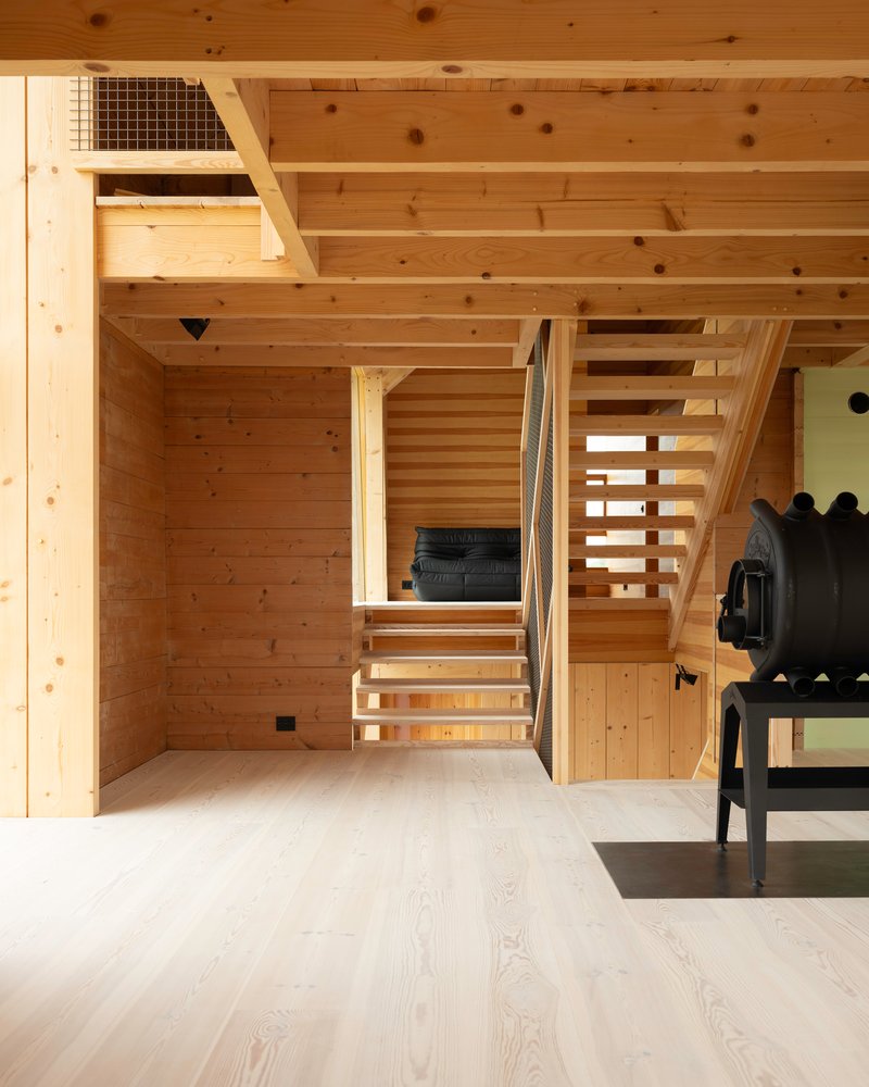 Open-tread timber staircase ascending between plank-clad walls and exposed ceiling joists