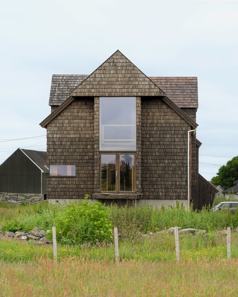 Front gable facade clad in dark shingles with a tall window overlooking grasses